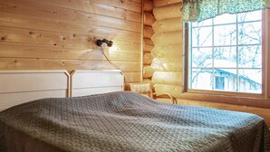 A wooden cabin room with a bed, a window, and a door.