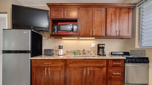 A kitchen with wooden cabinets, a refrigerator, a microwave, a stove, and a television above the microwave.