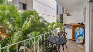 A balcony with a table and chairs, surrounded by lush green plants.