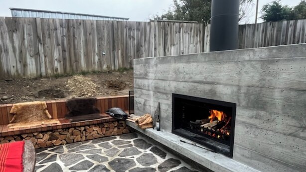 Un patio de piedra con chimenea integrada y un banco de madera.