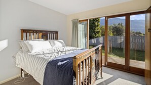 Un dormitorio con cama, cabecera de madera, amplia puerta corrediza de vidrio que da a un jardín trasero y vistas a montañas.