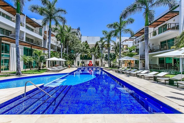 A swimming pool with steps leading into it, surrounded by palm trees and lounge chairs.