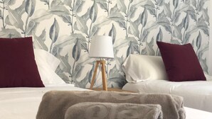 A neatly made bed with a white and gray patterned wallpaper, two red pillows, a white lamp on a wooden stand, and a gray towel on the bed. - Tetuan 3I - Two Bedroom Apartment, Sleeps 4 (Sevilla)