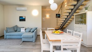 Ein modernes Wohnzimmer mit einer Couch, einem Esstisch mit Stühlen, einer Treppe und einer Küchenzeile mit Schränken.