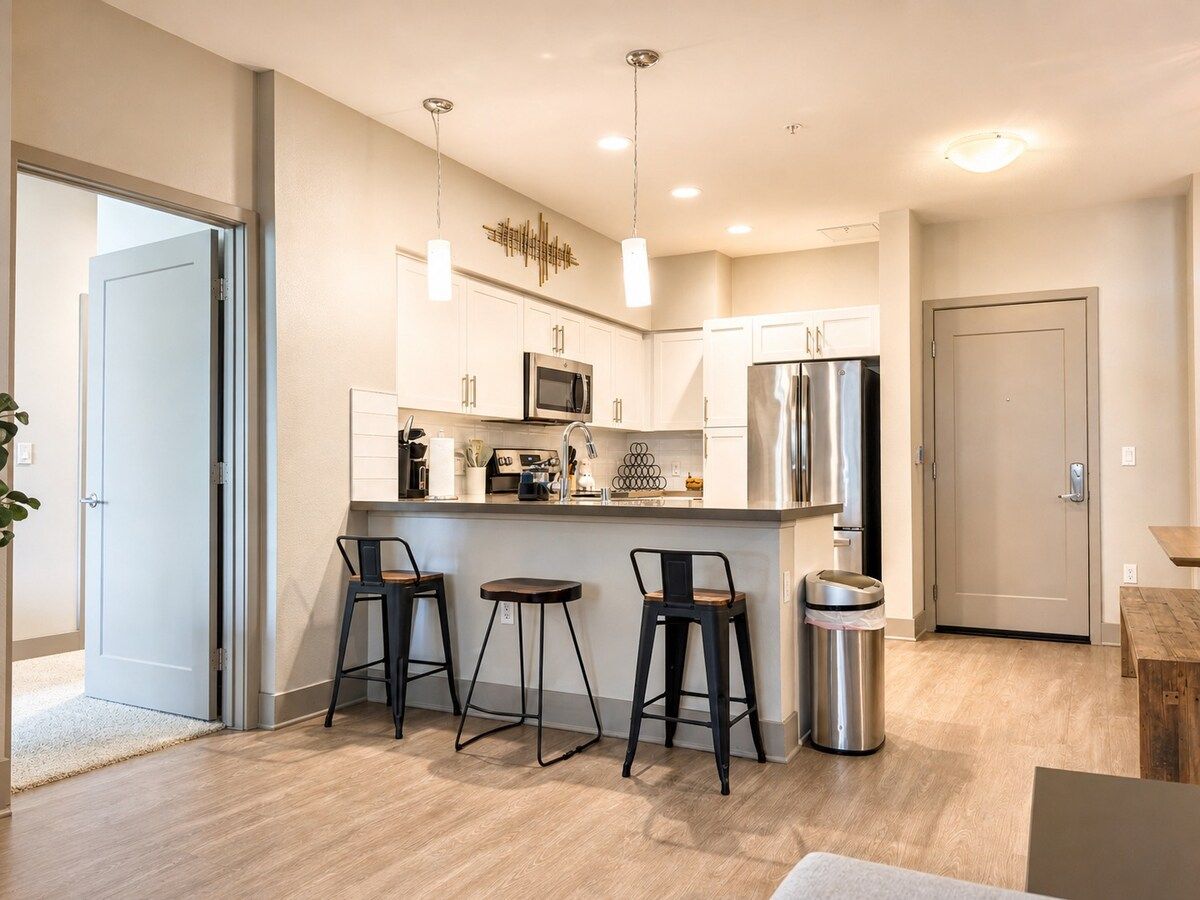 A modern kitchen with white cabinets, stainless steel appliances, and a bar area with stools.