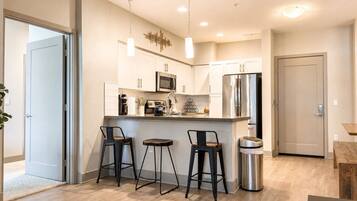 A modern kitchen with white cabinets, stainless steel appliances, and a bar area with stools.