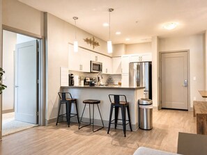 Une cuisine moderne avec des meubles blancs, des appareils en acier inoxydable et un coin bar avec des tabourets.