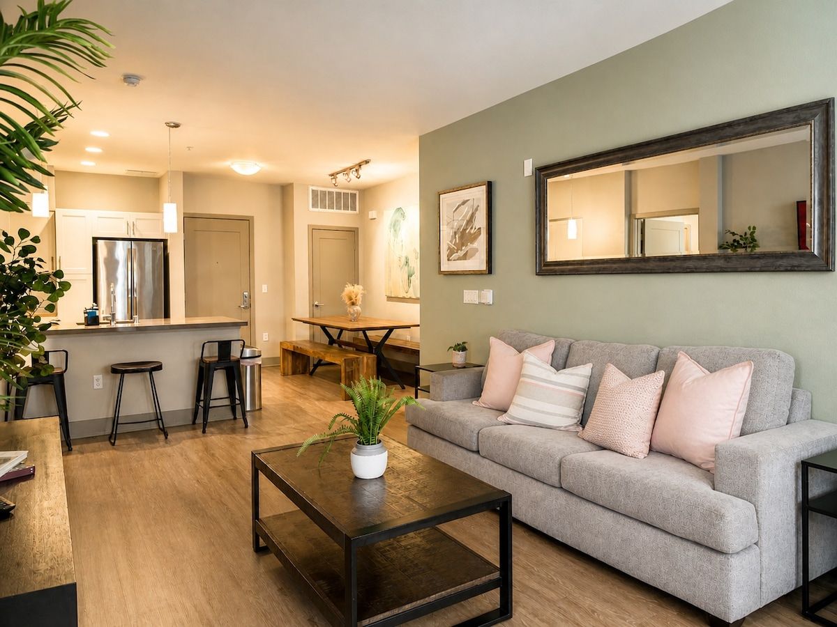 A living room with a grey sofa, a coffee table, and a kitchen in the background.
