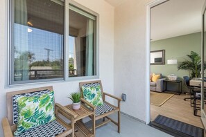 Un balcon avec deux chaises en bois, une petite table ornée d’une plante et une vue sur l’extérieur.