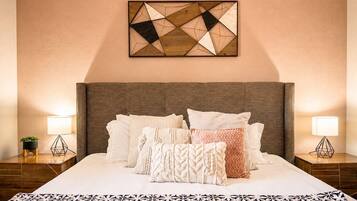 Ein Hotelzimmer mit einem großen Bett, vielen Kissen, einer geometrischen Wanddekoration und Nachttischlampen.