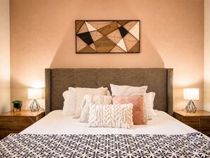 A hotel room with a large bed, multiple pillows, a geometric wall art piece, and bedside lamps.