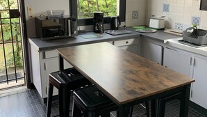 A modern kitchen with a wooden table, black stools, a coffee maker, and a window with a view of greenery. - Great House Montalivet (Vendays-Montalivet)