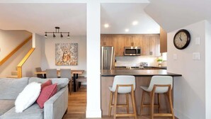 Une cuisine moderne avec des meubles en bois, des appareils en acier inoxydable et un coin bar avec des tabourets.