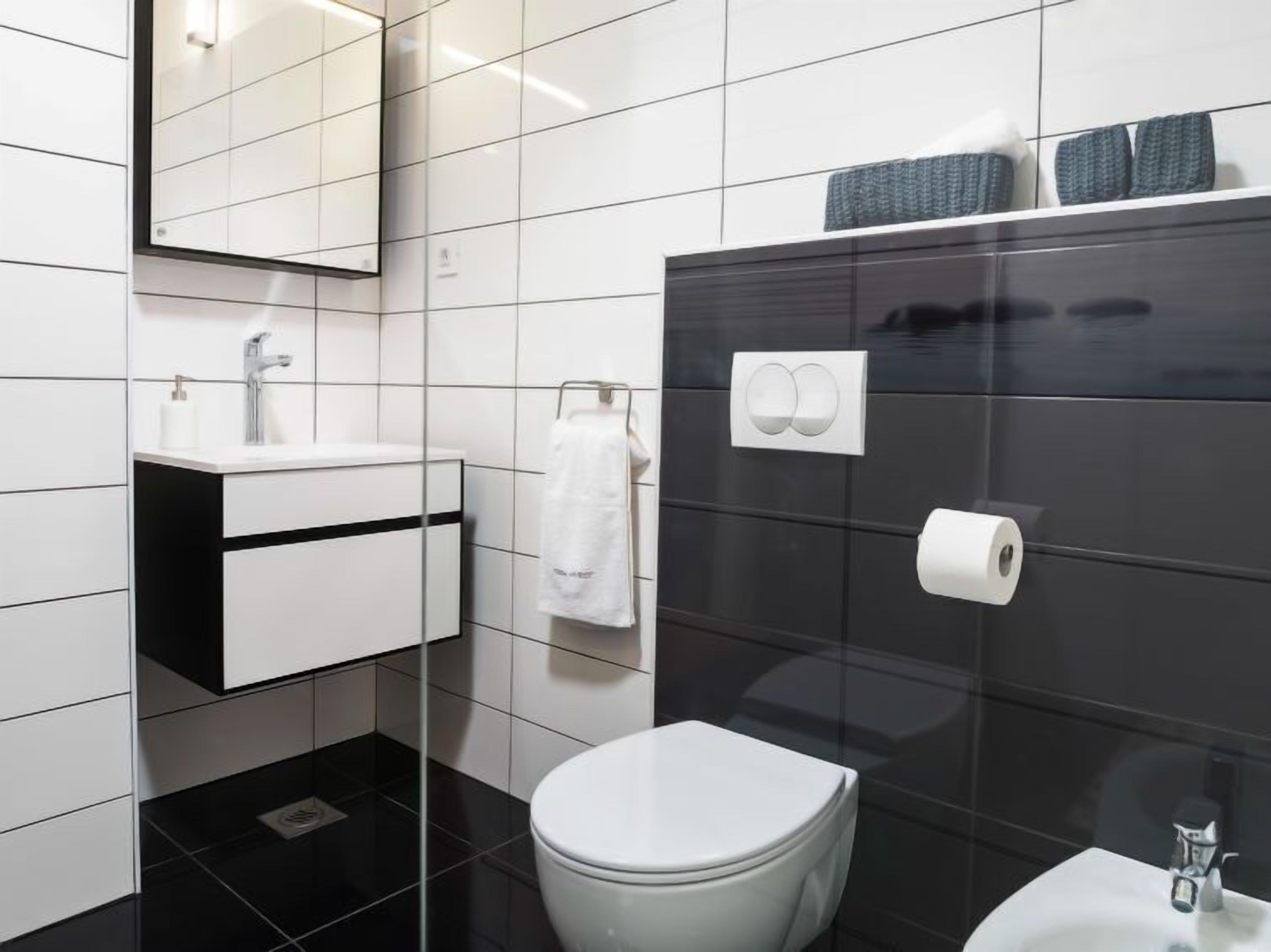 A modern bathroom with a black and white tiled wall, a white toilet, a sink with a mirror, and a towel rack.