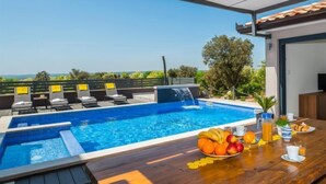 A poolside area with a wooden table set for breakfast, a pool with a waterfall feature, and lounge chairs. - Vacation home A.R.T. by Interhome (Labin)