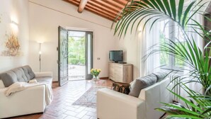 Un salón amplio con techo alto, un televisor sobre un mueble de madera y un ventanal con vistas al verdor.