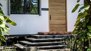 A modern building with a wooden door, steps leading to a porch, and a window overlooking greenery. - Eco Casita 3.2 - Casa de Olas (Hacienda Iguana)