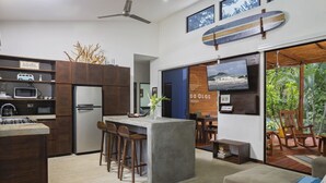 A modern kitchen with a central island, bar stools, and a dining area with a view of the outdoors. - Eco Casita 3.2 - Casa de Olas (Hacienda Iguana)