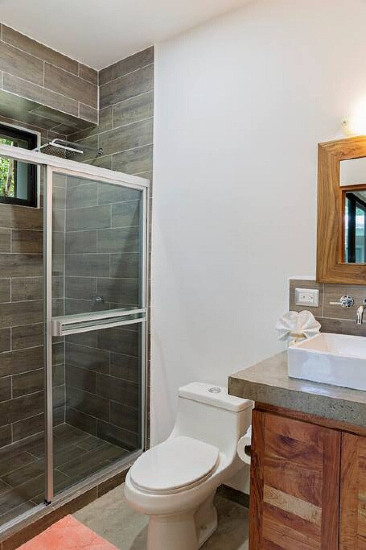 A bathroom with a glass-enclosed shower, a white toilet, and a wooden vanity with a mirror.