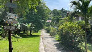 Un sendero atraviesa un jardín exuberante con indicaciones hacia casas, un restaurante y una zona tropical.