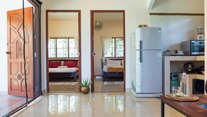 Amplia sala de estar con un gran ventanal corredero, una zona de cocina con refrigerador y una mesa de comedor.