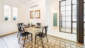 A dining area with a table set for four, black chairs, a patterned floor, and a large sliding glass door leading to an outdoor area. - Genteel Home Velazquez II (Madrid)