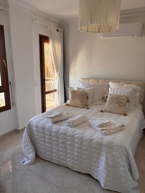 A neatly made bed with pillows and folded towels, a window with curtains, and a hanging light fixture. - Charming 3/4 bedroomed Villa with private pool and stunning rooftop terrace (Kalkan)
