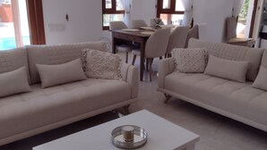 Een moderne woonkamer met twee beige banken, een witte salontafel en een eethoek met een houten tafel en stoelen.