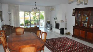 A dining area with a round wooden table and chairs, a patterned rug, a fireplace, and a bookshelf. - 4-rooms 145m3  ap. Seaside Athens: Glifada (Glifada)