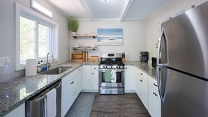 Eine moderne Küche mit weißen Schränken, Edelstahlgeräten, einer Arbeitsplatte aus Granit und Meerblick durch ein Fenster.