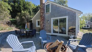 Eine Terrasse mit Adirondack-Stühlen, einer Feuerstelle und einem Esstisch mit Stühlen.