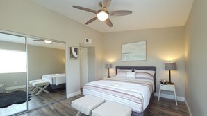 Ein modernes Schlafzimmer mit einem großen Bett, Nachttischlampen, einem Deckenventilator, einem Spiegel und Blick ins Freie.