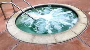 Ein Whirlpool mit einer Metallleiter, umgeben von einer gefliesten Terrasse.