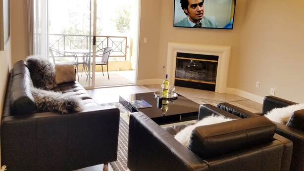 Ein Wohnzimmer mit einer Couch, einem Couchtisch mit Flasche und Glas, einem Kamin und einem an der Wand befestigten Fernseher.