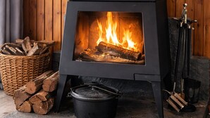 A wood-burning stove with logs, a basket of firewood, and a stone base. - Hilltop Hideaway, Firepit, Starry Nights & Privacy (Mullamuddy)