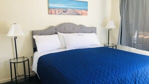 Habitación de hotel con una cama grande, dos lámparas de noche, un cuadro en la pared y una ventana con cortinas.