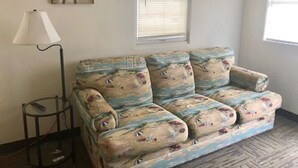 Una habitación con sofá, lámpara, un cuadro de un muelle y ventana con persianas.