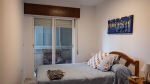 A bedroom with a bed, a nightstand, a lamp, a painting, and a sliding glass door leading to a balcony. - Everything ready to enjoy the summer, swimming pools, near the sea, tennis and more... (Torrevieja)