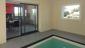 Een kamer met een zwembad, een schuifdeur naar een eetgedeelte en een raam met uitzicht op groen.