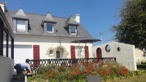 Een huis met een schuin dak, een stenen muur met ronde ramen en een tuin vol rode bloemen.
