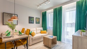A modern living room with a sofa, dining table, and coffee table. There are green curtains, a plant, and artwork on the walls.