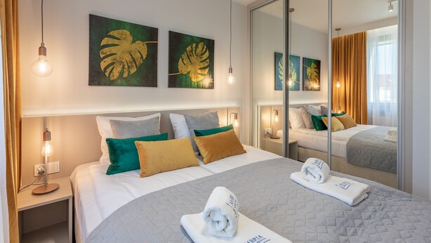 A hotel room with a bed, two bedside tables, a mirror, and artwork on the wall.