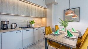 A modern kitchen with a wooden countertop, a sink, and a coffee maker. There is a dining table with yellow chairs and a mirror above it.