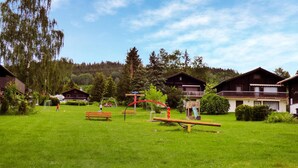 Ett grönområde med lekutrustning, bänkar och trähus med balkonger.