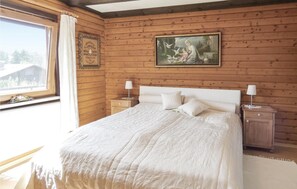 Un dormitorio con pared de paneles de madera, una cama grande con ropa blanca, dos mesitas de noche con lámparas, y un cuadro enmarcado sobre la cama.