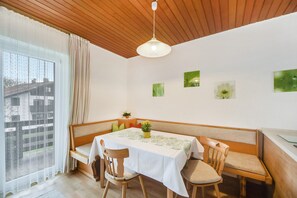 A dining area with a table, chairs, a bench, a hanging light fixture, and a window with curtains.