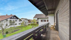 Un balcón de madera con vista a casas vecinas y un césped verde.