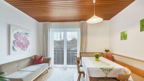 Una habitación con techo de madera, un sofá, una mesa de comedor con mantel y una ventana con cortinas.