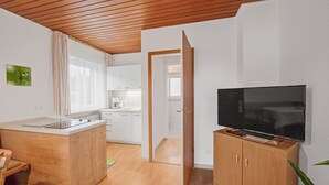 Una cocina moderna con armarios de madera, una zona de comedor con una silla y un televisor sobre un mueble de madera.