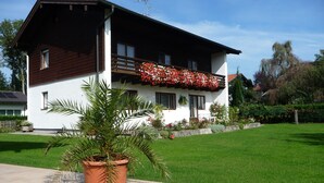 Una casa de dos pisos con un balcón, un jardín y una planta en maceta al frente.